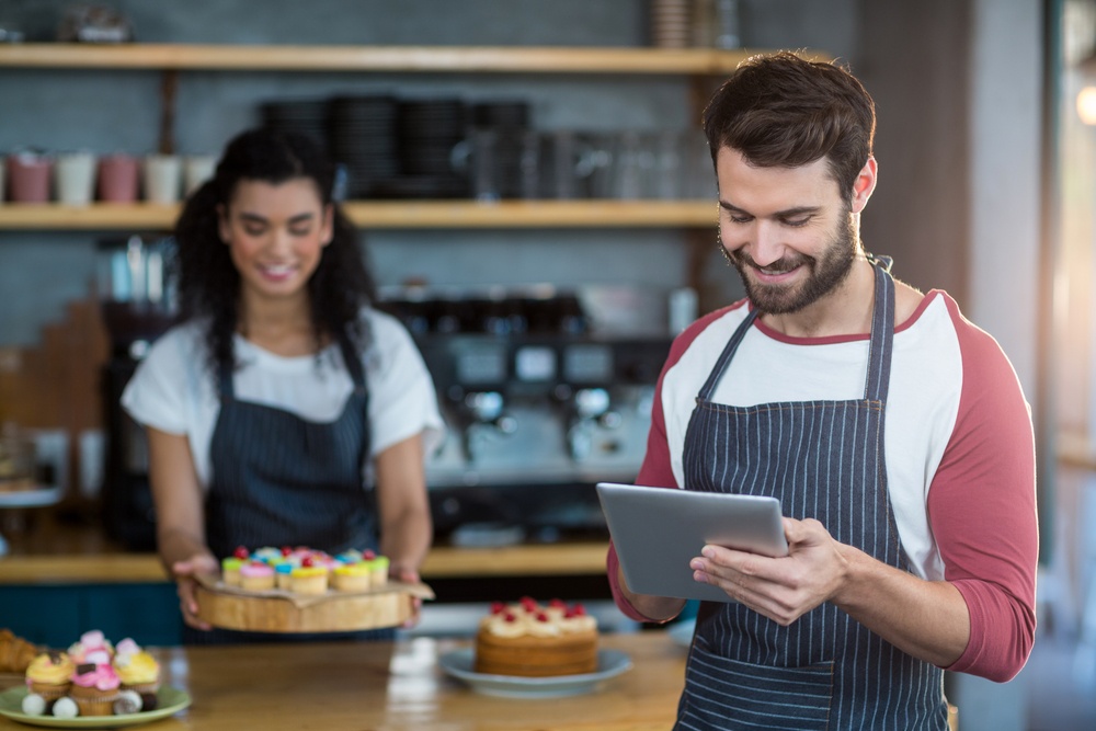 Smiling waiter using digital tablet at counter in cafx92xA9.jpeg